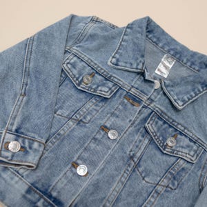 Puede incluir: Una chaqueta vaquera azul claro de dise&ntilde;o cl&aacute;sico, con cierre de botones, dos bolsillos en el pecho y mangas largas.
