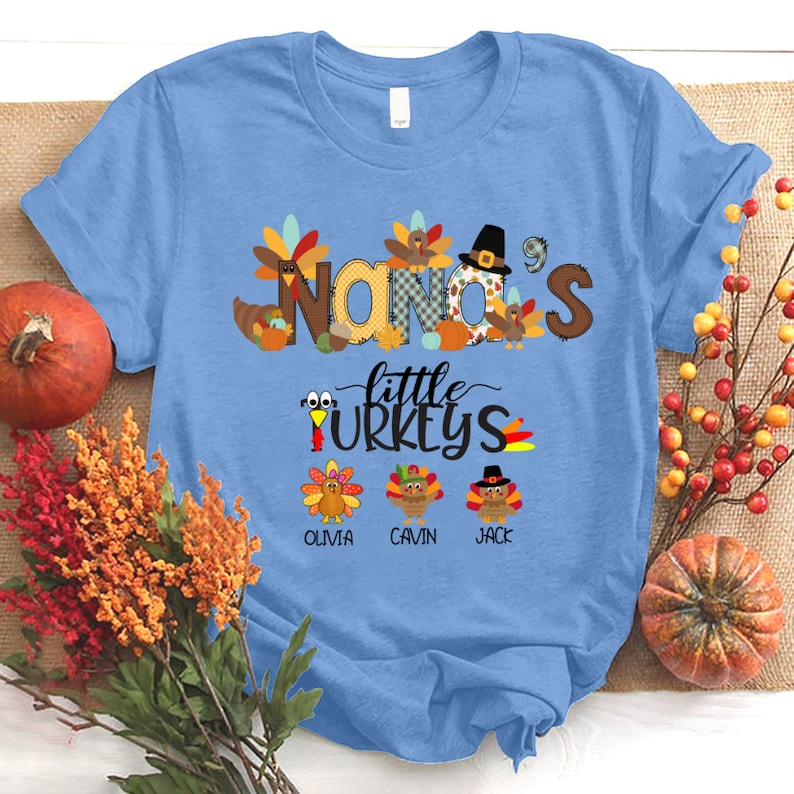 May include: A light blue t-shirt with the text "NANA'S little TURKEYS" in a patchwork style.  Three turkeys with names "OLIVIA", "CAVIN", and "JACK" are below the text.