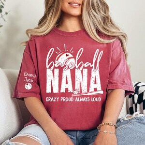 Peut inclure: T-shirt bordeaux avec l'inscription blanche &laquo;&nbsp;baseball NANA&nbsp;&raquo;, un motif de baseball et de c&oelig;ur. Le texte &laquo;&nbsp;CRAZY PROUD ALWAYS LOUD&nbsp;&raquo; est en dessous. La manche gauche porte le nom &laquo;&nbsp;Emma Jack&nbsp;&raquo; et un graphisme de baseball.