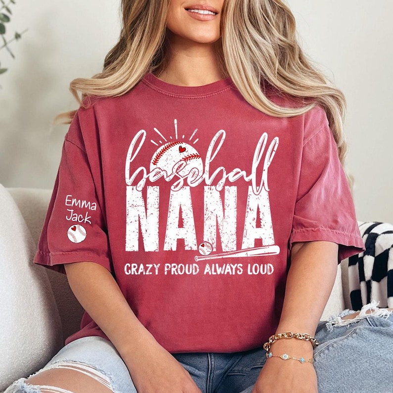Peut inclure: T-shirt bordeaux avec l'inscription blanche &laquo;&nbsp;baseball NANA&nbsp;&raquo;, un motif de baseball et de c&oelig;ur. Le texte &laquo;&nbsp;CRAZY PROUD ALWAYS LOUD&nbsp;&raquo; est en dessous. La manche gauche porte le nom &laquo;&nbsp;Emma Jack&nbsp;&raquo; et un graphisme de baseball.