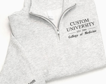 May include: A light gray quarter-zip sweatshirt with the text "CUSTOM UNIVERSITY EST. 2006 College of Medicine" printed in black. The sleeve cuff has the text "Custom Name" printed in black.