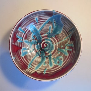 May include: A ceramic bowl with a red, white and blue swirl design. The bowl has a white base with a red swirl pattern and blue accents.