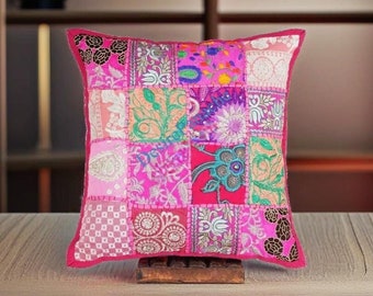 May include: A pink patchwork cushion cover with colorful floral embroidery and sequins. The cushion is square and has a fringed edge.