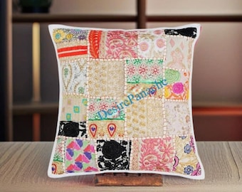 May include: A white square pillow with a patchwork design. The pillow is made of different fabrics in various colors, including red, pink, green, blue, and black. The fabrics are sewn together in a random pattern, creating a unique and colorful design. The pillow has a white border and is filled with a soft, comfortable material.