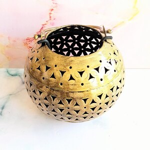 May include: A gold metal candle lantern with a decorative cut-out design. The lantern is round and has a handle on the top.