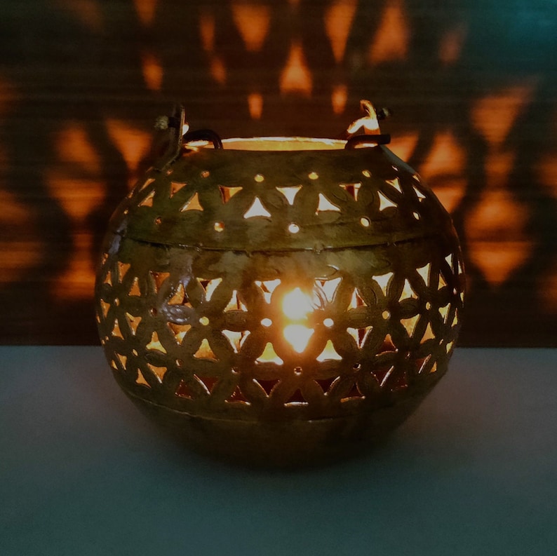 May include: A gold metal candle lantern with a decorative cut-out design. The lantern is round and has a handle on the top.