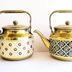 May include: Two gold tea kettles with ornate floral patterns. One kettle has a white background with red flowers, the other has a blue background with red flowers.