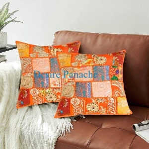 Puede incluir: Dos cojines de patchwork naranja y marrón con un diseño floral. Los cojines están en un sofá de cuero marrón.