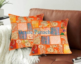 May include: Two orange and brown patchwork throw pillows with a floral design. The pillows are on a brown leather couch.