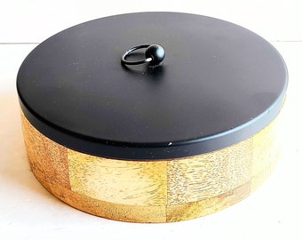 Puede incluir: Una caja redonda de madera con una tapa negra y una perilla negra. La caja tiene un acabado de madera natural y está hecha de madera.