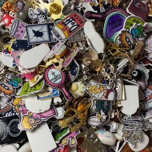May include: A large collection of colourful charms and pendants, including cartoon characters, animals, and abstract designs. Many of the charms are made of plastic and feature bright colours and whimsical details. The charms are perfect for adding a personal touch to jewellery, bags, or other accessories.