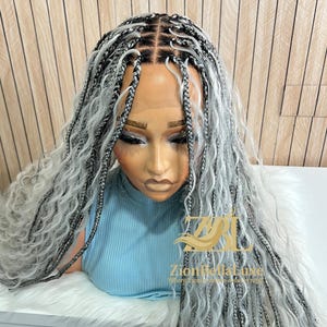 May include: A gray and black braided wig with long, wavy ends. The wig is styled on a mannequin head wearing a light blue top. The text "Zion Bella Line" is visible on the right side.