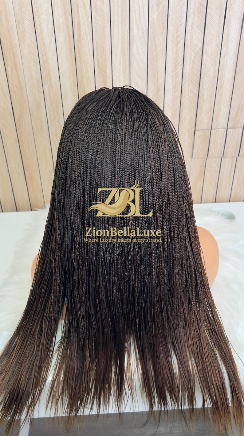 Op de afbeelding: Een donkerbruine pruik met lange, dunne, micro-gevlochten haarstrengen. De pruik wordt getoond op een etalagepophoofd en is voorzien van een gouden logo-overlay met de tekst ZBL ZionBellaLuxe Where Luxury meets every strand.