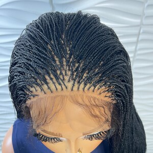 Op de afbeelding: Een zwarte lace front pruik met micro-vlechtjes in een strak, gescheiden ontwerp. De pruik heeft een transparante kanten basis bij de haarlijn, met ingewikkelde, fijne vlechten die vanaf de hoofdhuid naar buiten komen voor een uniforme textuur.