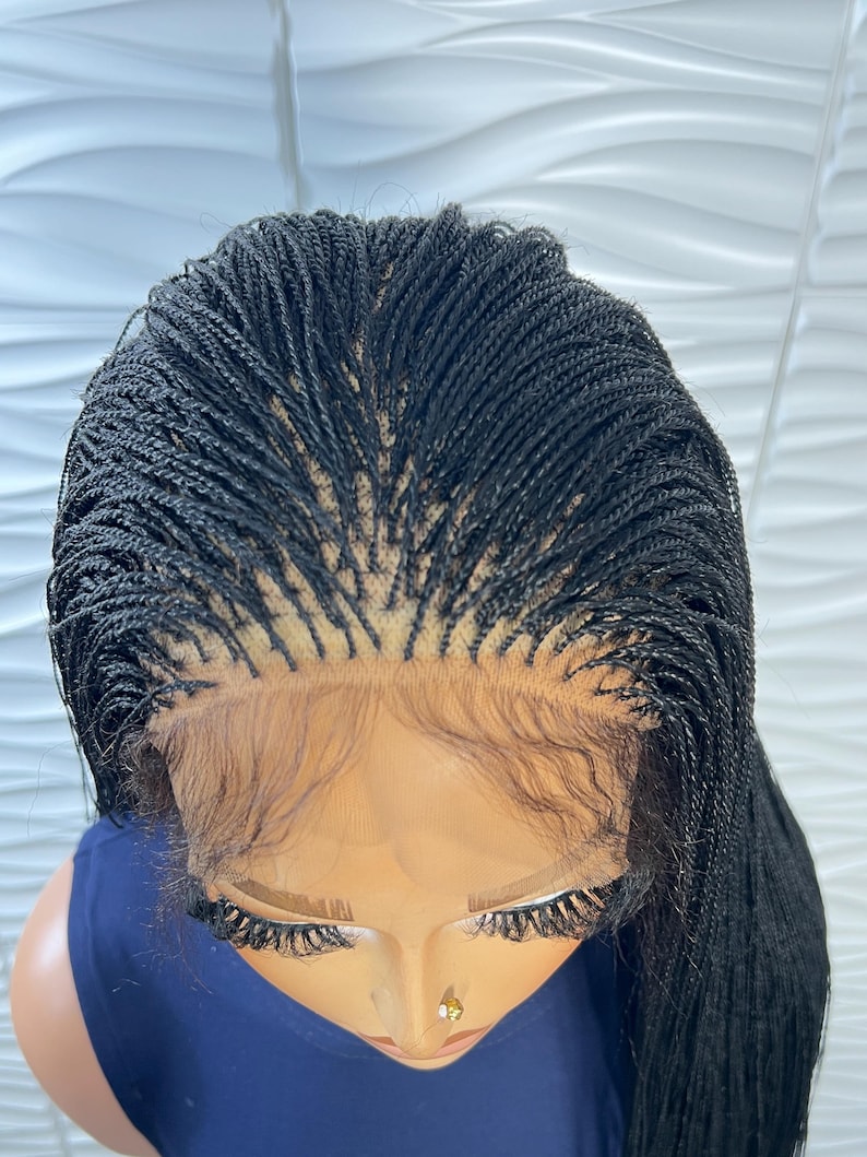 Op de afbeelding: Een zwarte lace front pruik met micro-vlechtjes in een strak, gescheiden ontwerp. De pruik heeft een transparante kanten basis bij de haarlijn, met ingewikkelde, fijne vlechten die vanaf de hoofdhuid naar buiten komen voor een uniforme textuur.