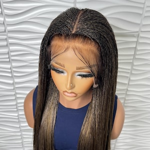 May include: A long, dark brown wig with blonde highlights, styled with a center part. The wig is on a mannequin head with a dark blue top. The background is a white, textured wall.