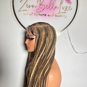 May include: A long, straight, braided wig with blonde, brown, and black hair extensions. The wig is styled in a side parting and has a lace front.