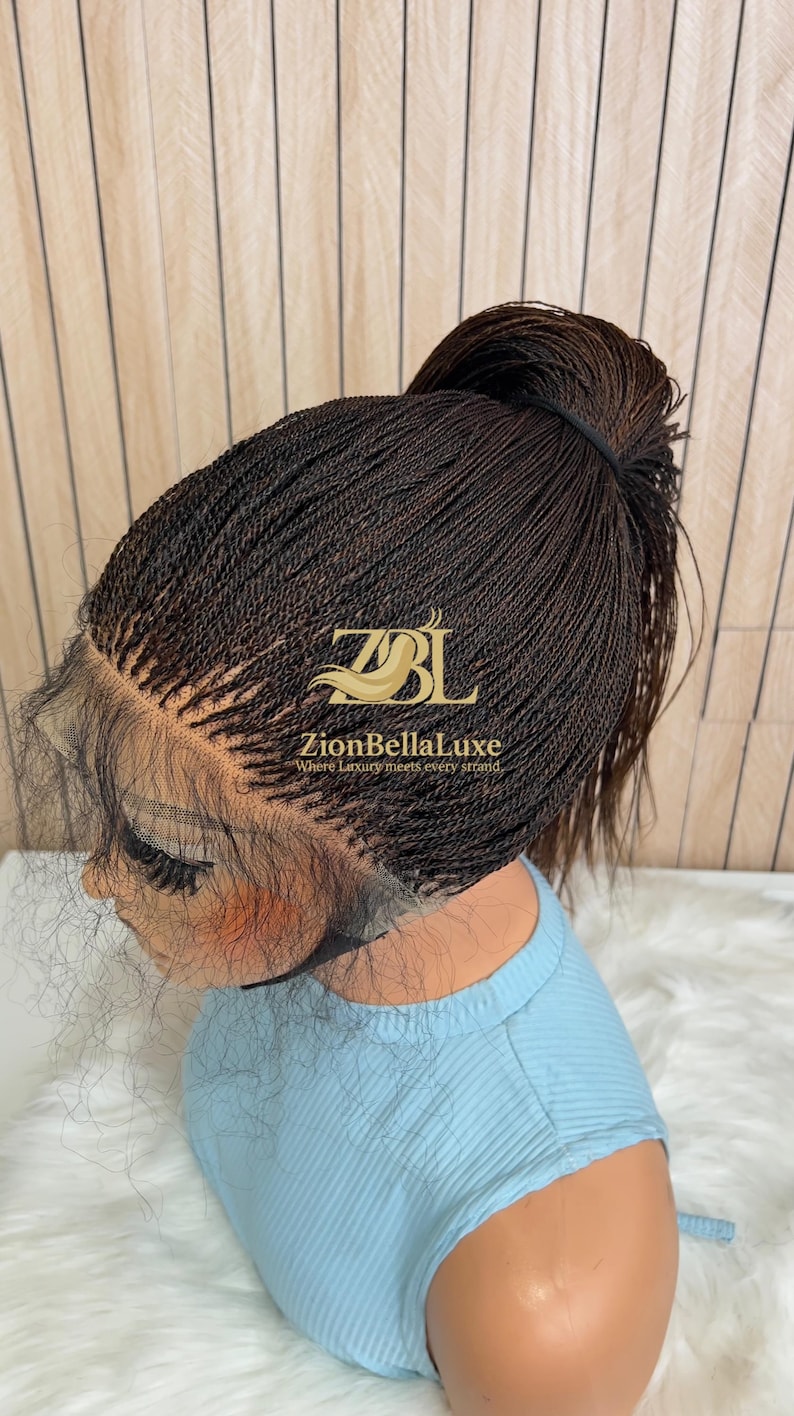 Op de afbeelding: Een donkerbruine lace front pruik gestyled in een hoge paardenstaart met micro-vlechtjes. De pruik heeft een transparante kanten haarlijn en is voorzien van de gouden tekst ZBL ZionBellaLuxe Where Luxury meets every strand op het vlechtwerk.