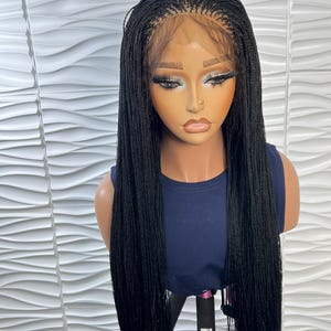 Op de afbeelding: Een lange, zwarte gevlochten pruik met micro-vlechten en een lace front haarlijn. De pruik wordt getoond op een etalagepop met een donkerblauw mouwloos topje. Het haar is recht, heeft een uniforme lengte en valt over de schouders.