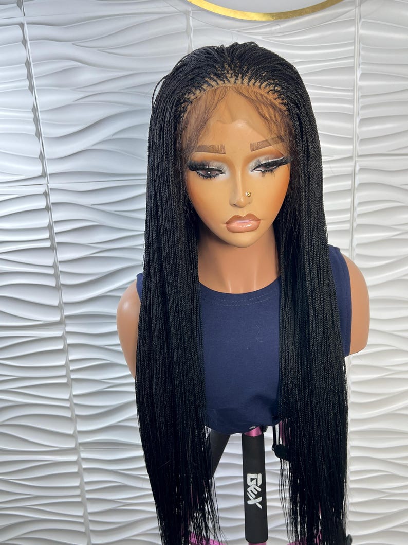Op de afbeelding: Een lange, zwarte gevlochten pruik met micro-vlechten en een lace front haarlijn. De pruik wordt getoond op een etalagepop met een donkerblauw mouwloos topje. Het haar is recht, heeft een uniforme lengte en valt over de schouders.