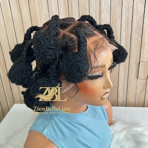 May include: A black wig styled with multiple looped sections. The wig is on a mannequin head wearing a light blue top. The logo "ZionBellaLuxe" is visible on the mannequin. The wig appears to be made of synthetic hair.