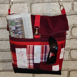 Könnte beinhalten: Eine rote und schwarze Patchwork-Stofftasche mit einem Reißverschlussfach und einer Zeitung darin. Die Tasche hat einen langen Riemen mit einem silbernen Verschluss.