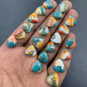 Puede incluir: Colección de piedras preciosas triangulares en varios colores, incluyendo turquesa, naranja, blanco y dorado. Las piedras se sostienen en una mano, mostrando sus patrones y texturas únicos. Ideales para la creación de joyas.