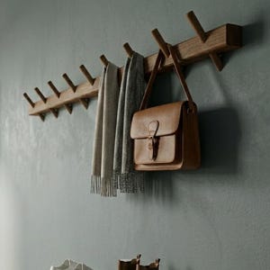 Könnte beinhalten: Ein hölzerner Eingangsbereich mit einer Wandgarderobe, einer braunen Ledertasche und einem Schuhregal. Die Garderobe hält Schals. Weiße Turnschuhe und braune Stiefel stehen auf dem Schuhregal. Ein kleiner Spiegel und eine Topfpflanze sind ebenfalls zu sehen.