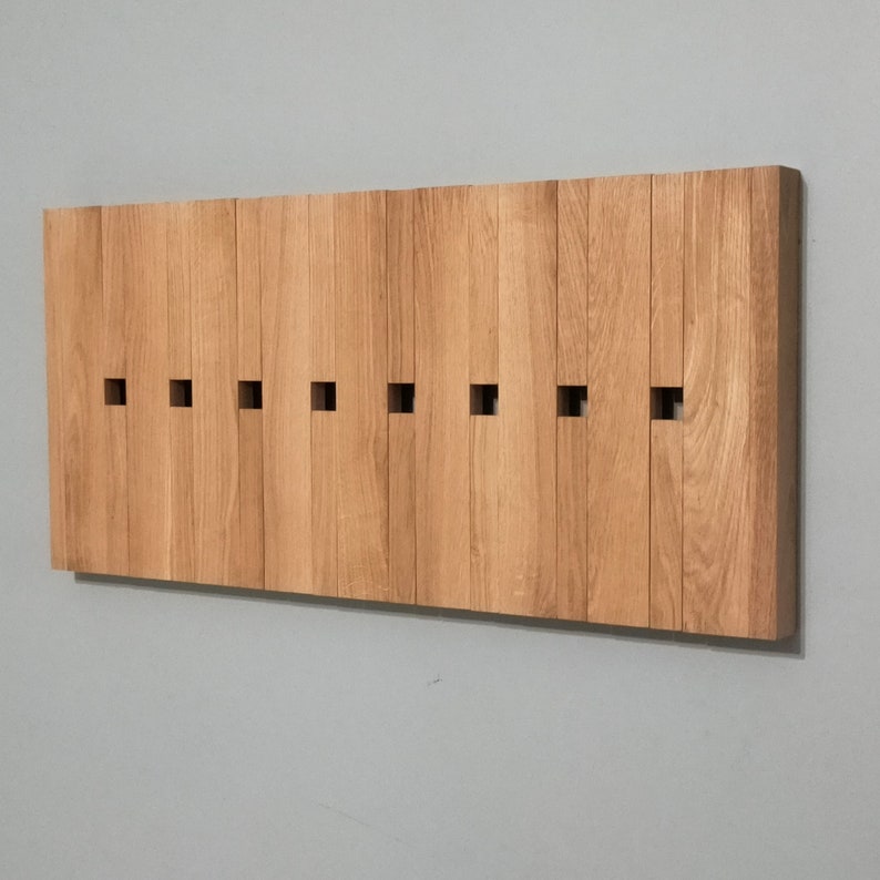May include: A wooden wall-mounted coat rack with a series of rectangular slots for hanging items. The rack is made of light brown wood and has a natural finish.