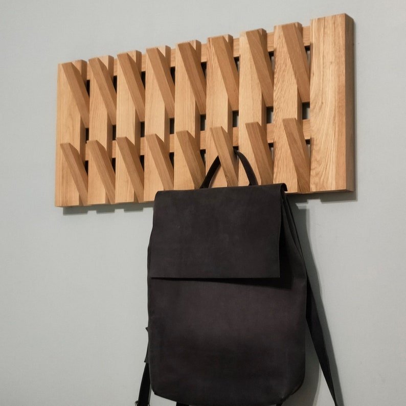 May include: A wooden wall-mounted coat rack with a geometric design. The rack has a black backpack hanging from it.