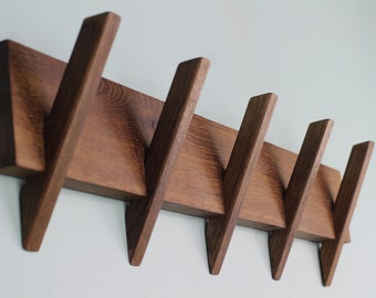 May include: A wooden wall-mounted coat rack with five angled hooks. The rack is made of dark brown wood and has a natural wood grain finish.