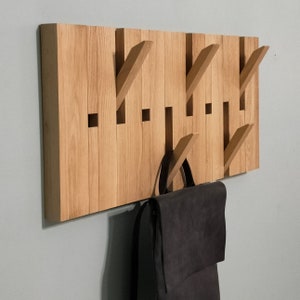 May include: A wooden wall-mounted coat rack with multiple hooks. The rack is made of light brown wood and has a natural finish. A black backpack is hanging on one of the hooks.