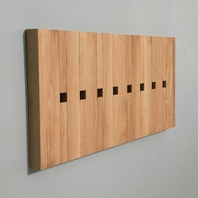 May include: A wooden wall-mounted coat rack with a series of rectangular cutouts. The rack is made of light brown wood and has a natural finish.