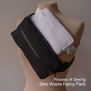 Puede incluir: Una riñonera negra y blanca con dos compartimentos con cremallera. La riñonera está hecha de un tejido suave y acolchado y se lleva en un maniquí.