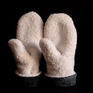 Könnte beinhalten: Ein Paar weiße Fleece-Handschuhe mit grünen Bündchen. Die Handschuhe sind weich und flauschig, perfekt um Ihre Hände im Winter warm zu halten.