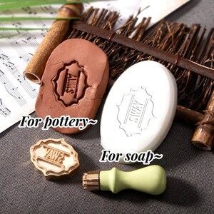 May include: An assortment of craft stamps for pottery and soap. The image shows a brown clay stamp with the word "SWAY", a white oval soap with the same design, and a gold and green stamp with the word "YAWS".