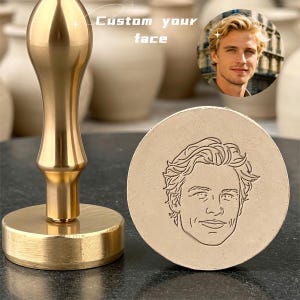Könnte beinhalten: Ein goldfarbener Wachssiegelstempel aus Metall mit langem Griff und kreisförmiger Basis. Der Stempelkopf zeigt eine detaillierte Strichzeichnung eines Gesichts. Der Text "Custom your face" ist im oberen Teil des Bildes zu sehen.