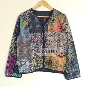 May include: A patchwork jacket with a V-neck and long sleeves. The jacket features a variety of fabric patterns in shades of blue, pink, green, and orange. The jacket is hanging on a wooden hanger.