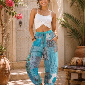 May include: A white sleeveless crop top with a front knot detail paired with loose-fitting blue patchwork trousers featuring various floral and geometric patterns, an elasticated waistband with a drawstring, and elasticated cuffs at the ankles.