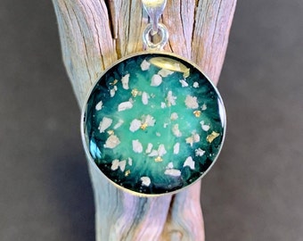 May include: A round silver pendant with a green and white resin inlay. The resin has a swirling pattern with white flecks and gold glitter.