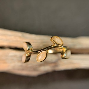May include: A gold ring with a delicate branch design and white leaves. The ring is made of metal and has a simple, elegant style.