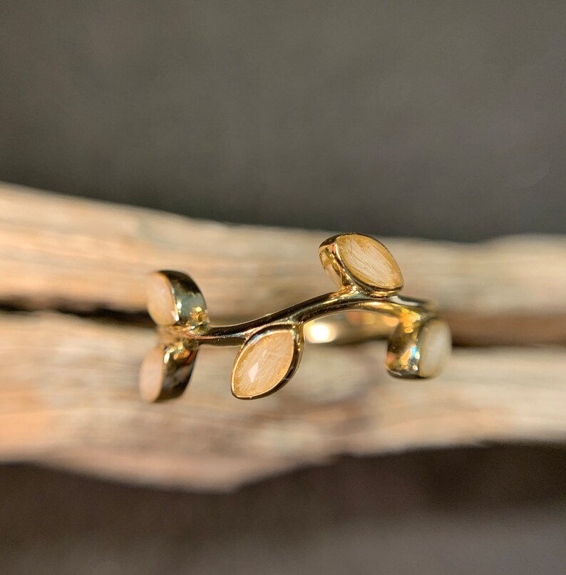 May include: A gold ring with a delicate branch design and white leaves. The ring is made of metal and has a simple, elegant style.