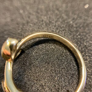 May include: Close-up of the inside of a gold ring with the inscription "G14K" on the band.