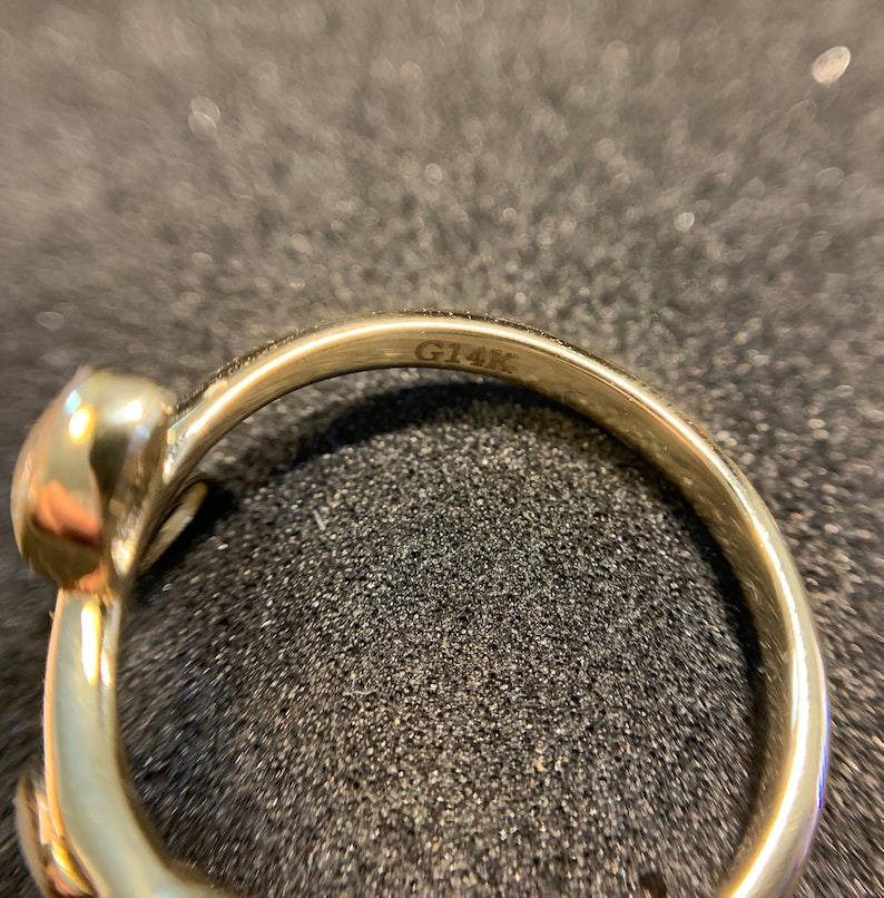 May include: Close-up of the inside of a gold ring with the inscription "G14K" on the band.
