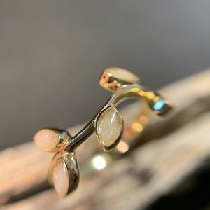 May include: A gold ring with a delicate branch design featuring four oval-shaped white stones.