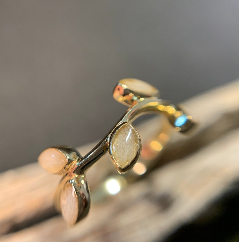 May include: A gold ring with a delicate branch design featuring four oval-shaped white stones.