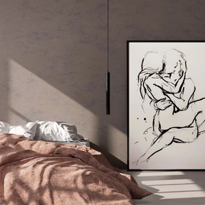 Pode incluir: Um desenho a preto e branco de duas pessoas a abra&ccedil;arem-se, enquadrado numa moldura preta e pendurado numa parede bege. Uma cama castanha com almofadas brancas est&aacute; em primeiro plano.