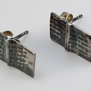 May include: A pair of silver book-shaped earrings with a hammered texture. The earrings have a silver post and a gold-toned butterfly back.