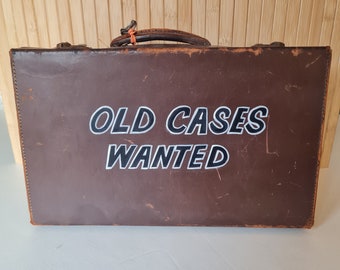 valise en cuir marron vintage avec lettres peintes à la main qui disent « Old Cases Wanted ».