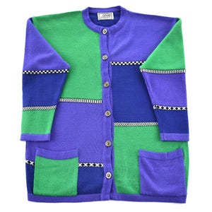 Può includere: Un cardigan a blocchi di colore nei toni del verde, blu e viola. Il maglione con bottoni presenta uno scollo tondo, maniche lunghe e due tasche anteriori. L'etichetta recita "Gianni Versace". Il design include motivi a scacchi e zigzag in bianco e nero.